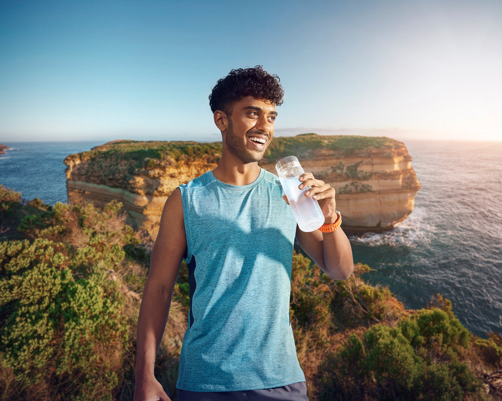 A man hydrates on a cliff, with a view of the ocean in the background.